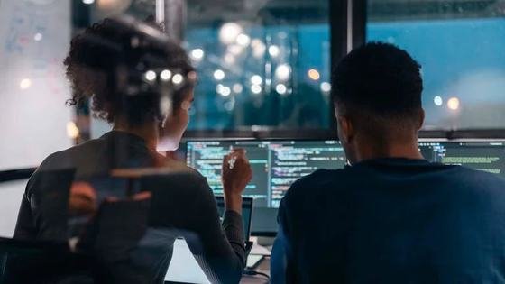 Two engineers reviewing code together at night