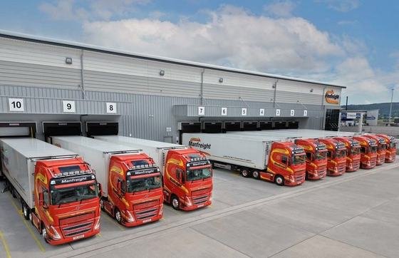 A fleet of red haulage trucks at a logistics warehouse