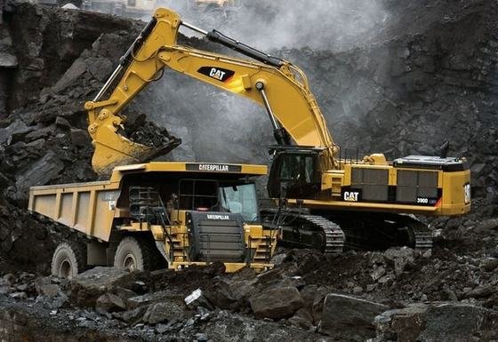 A mining excavator loading a haul truck at a rock face