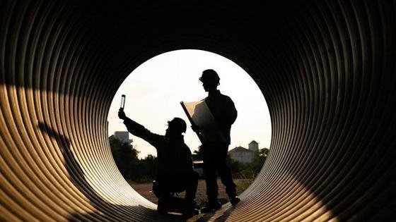 Two engineers silhouetted at the mouth of a large steel pipe