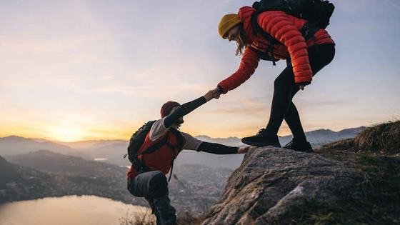 A climber reaching down to help a companion up a ridge at sunrise